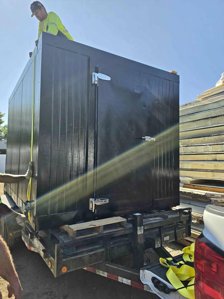 A crew member strapping a walk-in freezer onto a flatbed trailer
