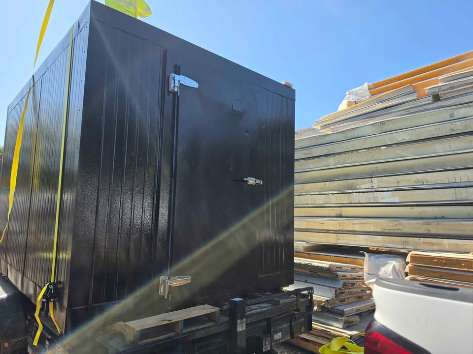 A black walk-in freezer strapped down on the trailer